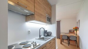 A modern kitchen with a built-in microwave, a coffee maker, and a sink. There is a dining area with two chairs and a table. - Cozy Stay Near Dunes (Julianadorp aan Zee)