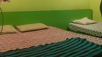 Une pièce avec un mur vert, un lit avec une literie à motifs, un climatiseur fixé au mur et un luminaire au plafond.