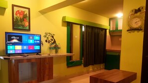 A modern kitchen with a built-in TV, wooden cabinets, a green-framed mirror, and a clock on the wall. - Godwill Kimo Guest House (Majorda)