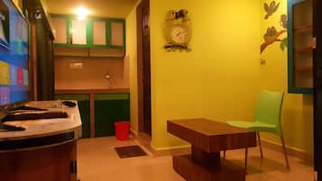 Um espaço compacto com cozinha compacta, uma mesa de madeira, uma cadeira verde e um relógio fixado na parede.