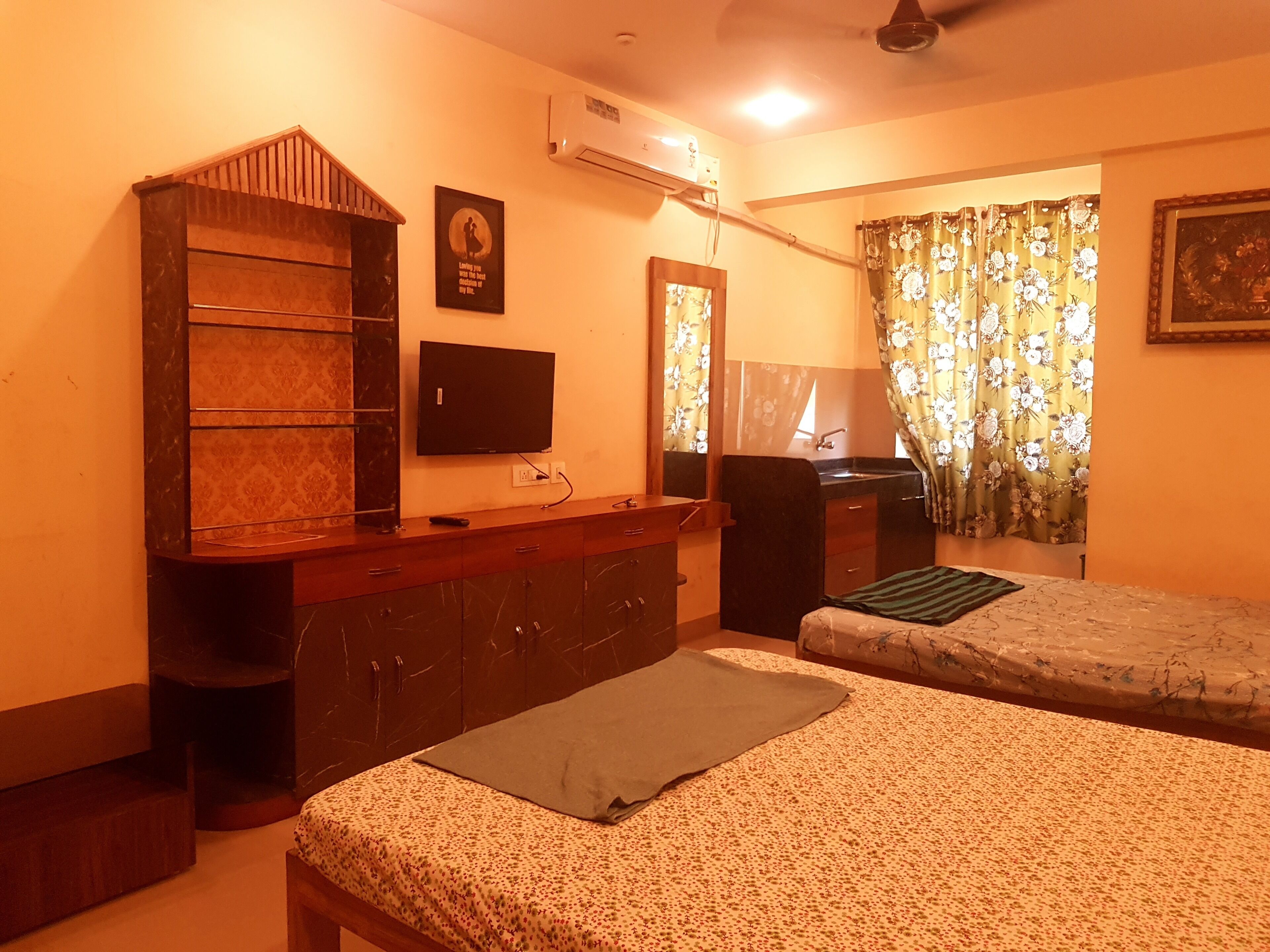Un dormitorio con una cama, cómoda, televisor, espejo y ventana con cortinas.