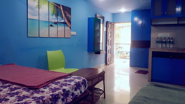 A room with a bed, a green chair, a desk, a television, and a wardrobe. - Godwill Kimo Guest House (Majorda)