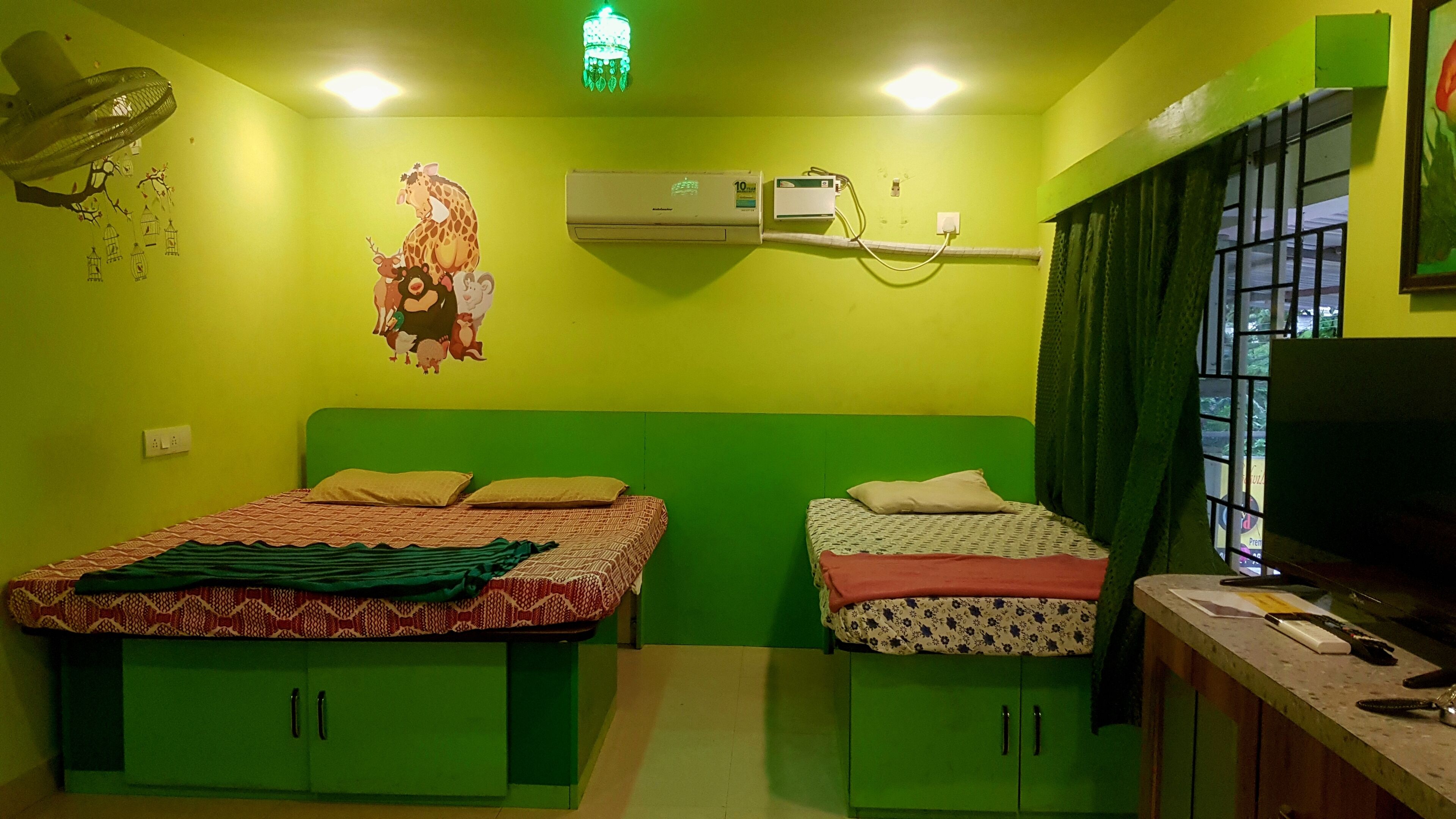 Una habitación con dos camas, armarios verdes, aire acondicionado, un adorno en la pared y una ventana con cortinas.
