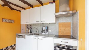 Una cocina con armarios blancos, una campana extractora de acero inoxidable, una cafetera y un lavavajillas.