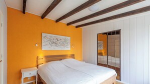 Un dormitorio con cama de madera, mesita de noche blanca y un ventanal con vistas a un balcón.
