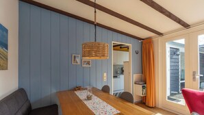 Un comedor con una mesa de madera, sillas, una lámpara colgante de fibra y vistas a la cocina por una puerta abierta.