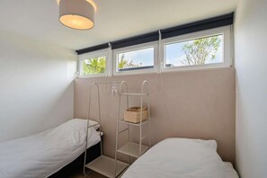 A room with two single beds, a window with a view of trees, and a shelf with a basket.