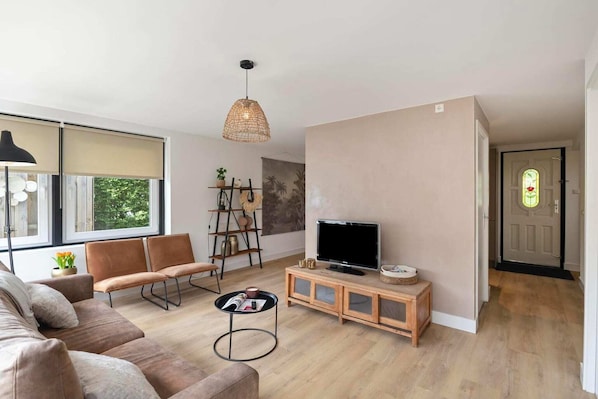A modern living room with a sofa, chairs, a coffee table, a TV, and a bookshelf.
