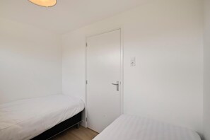 A small, single-room accommodation with two beds, a door, and a power outlet on the wall. - Bungalow in Sint Maartenszee near Sandy Beach (Sint Maartenszee)