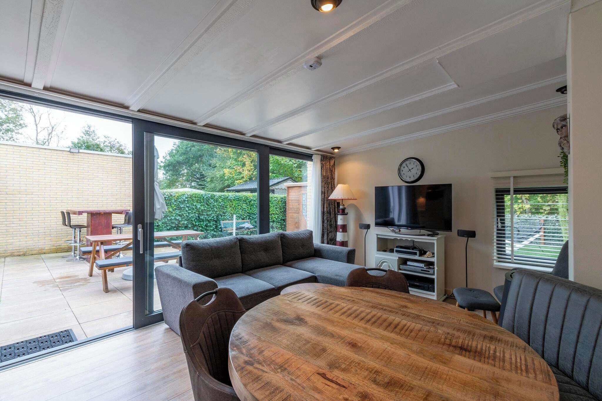 Una sala moderna con una mesa de comedor de madera, sofá gris y televisor sobre un mueble blanco.