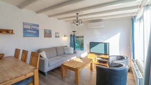 Ein Wohnzimmer mit Esstisch aus Holz, grauem Sofa und blauen Sesseln.