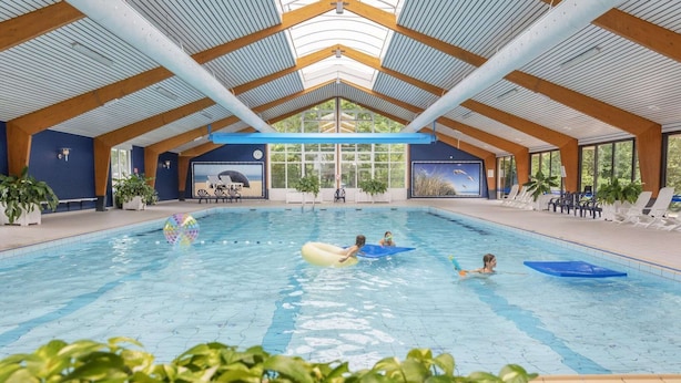 An indoor swimming pool with a high ceiling, wooden beams, and large windows. - Holiday Home near Dutch Beach with Pool (Sint Maartenszee)