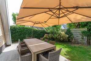 Eine Terrasse im Freien mit Tisch, Stühlen und einem großen Sonnenschirm, an einer Backsteinmauer.