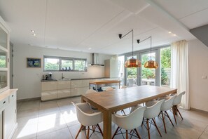 Eine moderne Küche mit Essbereich, großen Fenstern und Pendelleuchten.