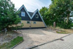 Una casa moderna con un diseño de techo triangular distintivo, camino de entrada de grava y un pequeño jardín.