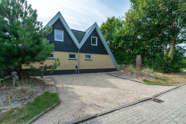Ein modernes Haus mit einem markanten, dreieckigen Dach, einer Schotterauffahrt und einem kleinen Garten.