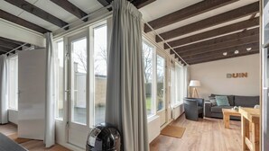 A modern living room with a grey sofa, a wooden table, and a black trash bin. - Duinland 245 bungalow for 6 guests near sea (Sint Maartenszee)