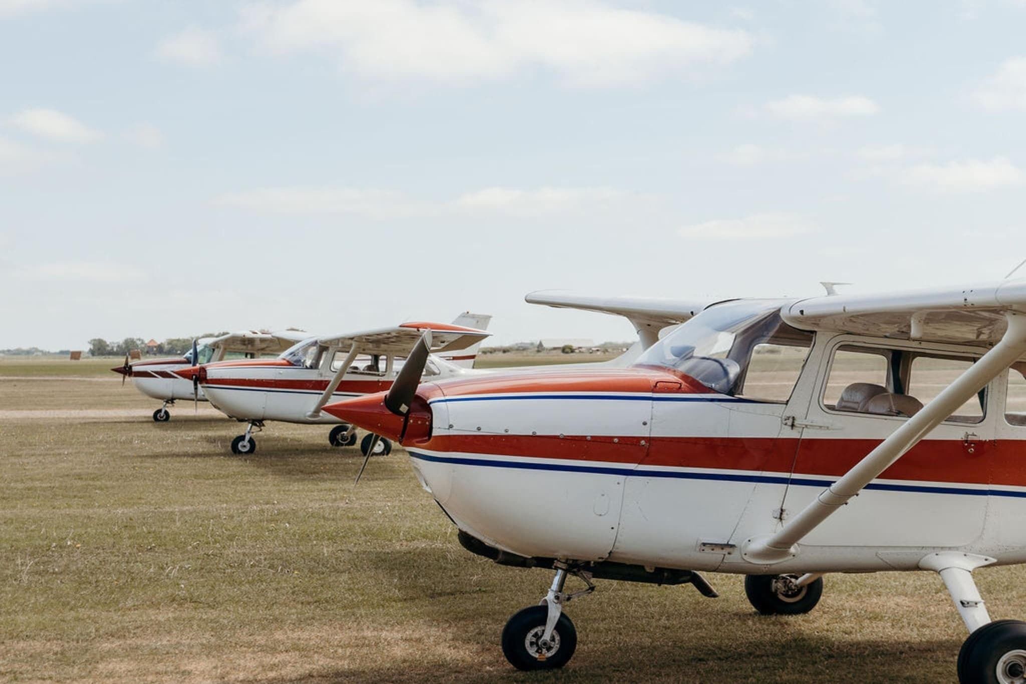 Una fila de aviones pequeños de un solo motor estacionados en un campo cubierto de hierba.