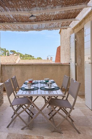 An outdoor patio with a table set for four, surrounded by chairs, under a woven shade structure. - Sur le Port de Hyères-5 min de la Plage-calme (Hyères)