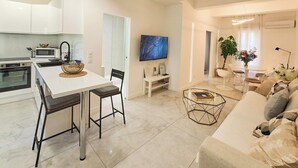 A modern kitchen with white cabinets, a dining area with a white table and chairs, a living room with a sofa and a coffee table, and a TV mounted on the wall. - La Perle du Mourillon-wifi-spacieux (Toulon)