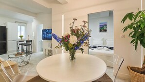 A modern living room with a round white table, clear chairs, a white sofa, a dining area with a small table and chairs, and a large window. - La Perle du Mourillon-wifi-spacieux (Toulon)