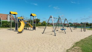 A playground with a yellow slide and swings, set on sandy ground with houses in the background. - Apartment 189 in Julianadorp aan Zee (Julianadorp aan Zee)