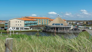 A waterfront hotel with a central building featuring balconies and a circular structure with a conical roof. - Strandslag 193 charming apartment for 4-person (Julianadorp aan Zee)
