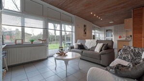 Un salón amplio con un ventanal grande, una mesa de centro blanca, un sofá gris y un sillón estampado.
