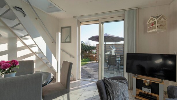 A modern living room with a flat-screen TV, comfortable seating, a staircase, and a sliding glass door leading to an outdoor area.