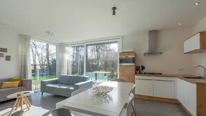 A modern kitchen with white cabinets, a built-in oven, and a stainless steel range hood. - Bungalow near Dutch Beach and Bulb Fields (Sint Maartensvlotbrug)