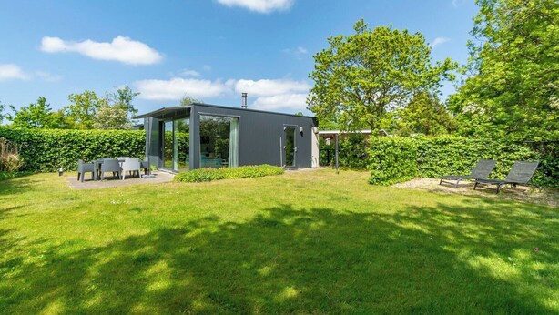 A modern house with a glass conservatory, a patio with a table and chairs, and a garden with a bench. - Bungalow near Dutch Beach and Bulb Fields (Sint Maartensvlotbrug)