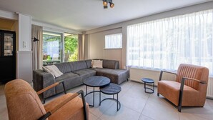Una sala moderna con un sofá modular, dos sillones y dos mesas de centro redondas.