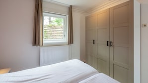 A bedroom with a bed, a window with curtains, a radiator, and a wardrobe. - Holiday home Effe Sprage in Callanstoog Centre (Callantsoog)