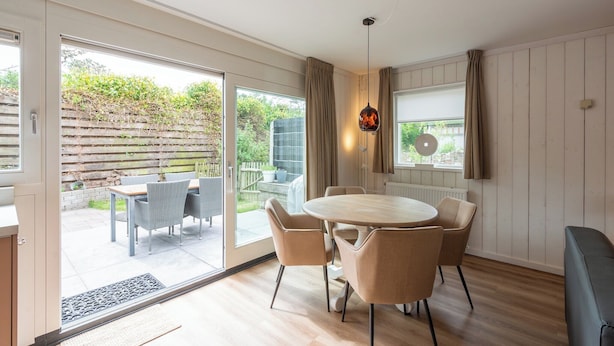 A modern kitchen with a large island, a dining area with a round table and chairs, and a sliding glass door leading to a patio. - Holiday home Effe Sprage in Callanstoog Centre (Callantsoog)
