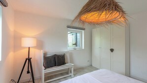 A bedroom with a bed, a bedside lamp, a bench, a wardrobe, and a window with a view. - Bungalow in Callantsoog near the Beach (Callantsoog)