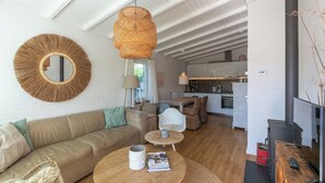 A cozy living room with a sofa, round coffee table, and a large mirror. There is a kitchen area with cabinets and a stove in the background. - Bungalow in Callantsoog near the Beach (Callantsoog)