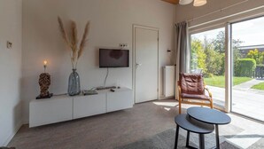 Ett modernt vardagsrum med en platt-TV som är monterad på väggen, ett vitt konsolbord med dekorativa föremål, en läderfåtölj och ett litet runt bord.
