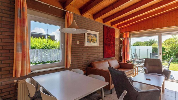 A cozy room with a brick wall, wooden ceiling beams, a white table, and leather seating. - Bungalow near Beach and Forest in De Blenck (Callantsoog)