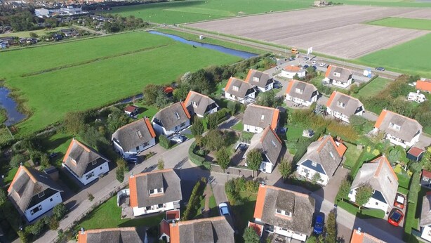 An aerial view of a residential area with houses, green fields, and a small water body.