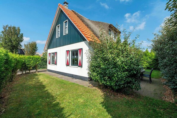 A house with a steeply pitched roof, white exterior walls, and red shutters.