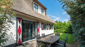 A house with a thatched roof, white exterior walls, and a wooden table with chairs outside.