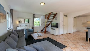 A modern living room with a sofa, a TV, and a staircase leading to a kitchen.