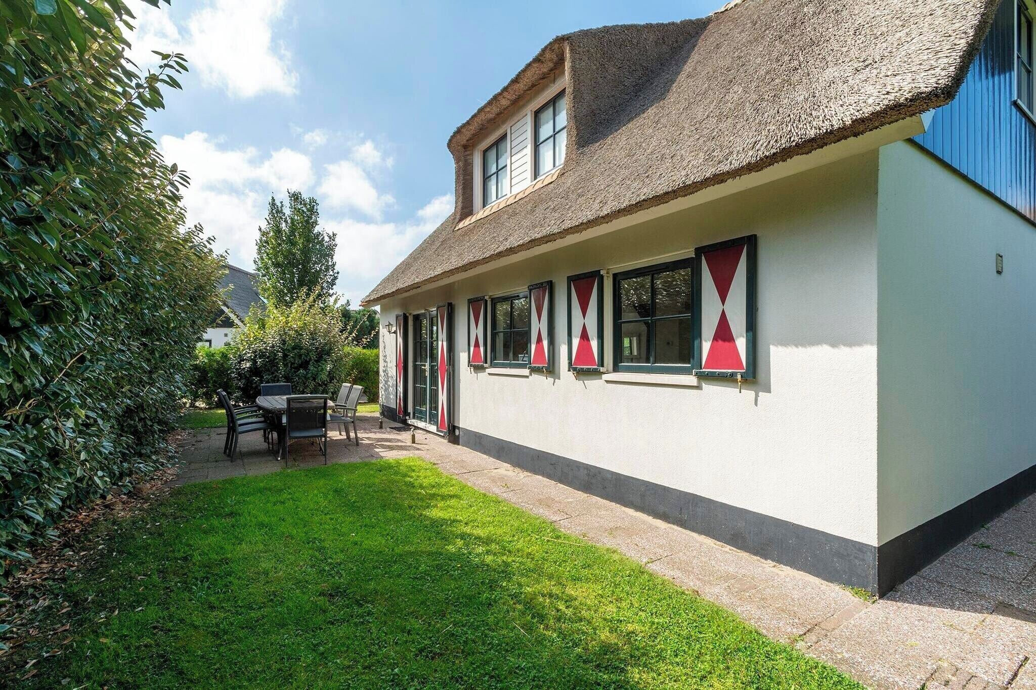 A building with a thatched roof, white walls, and red triangular window frames.