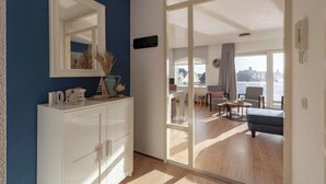 A modern living room with a large sliding glass door leading to a balcony, a white cabinet with decorative items, and a large mirror on the wall.