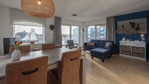 A modern living room with a dining area, large windows, and a view of a sailboat.