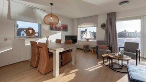 A modern living room with a dining area, large windows, and a view of the cityscape.