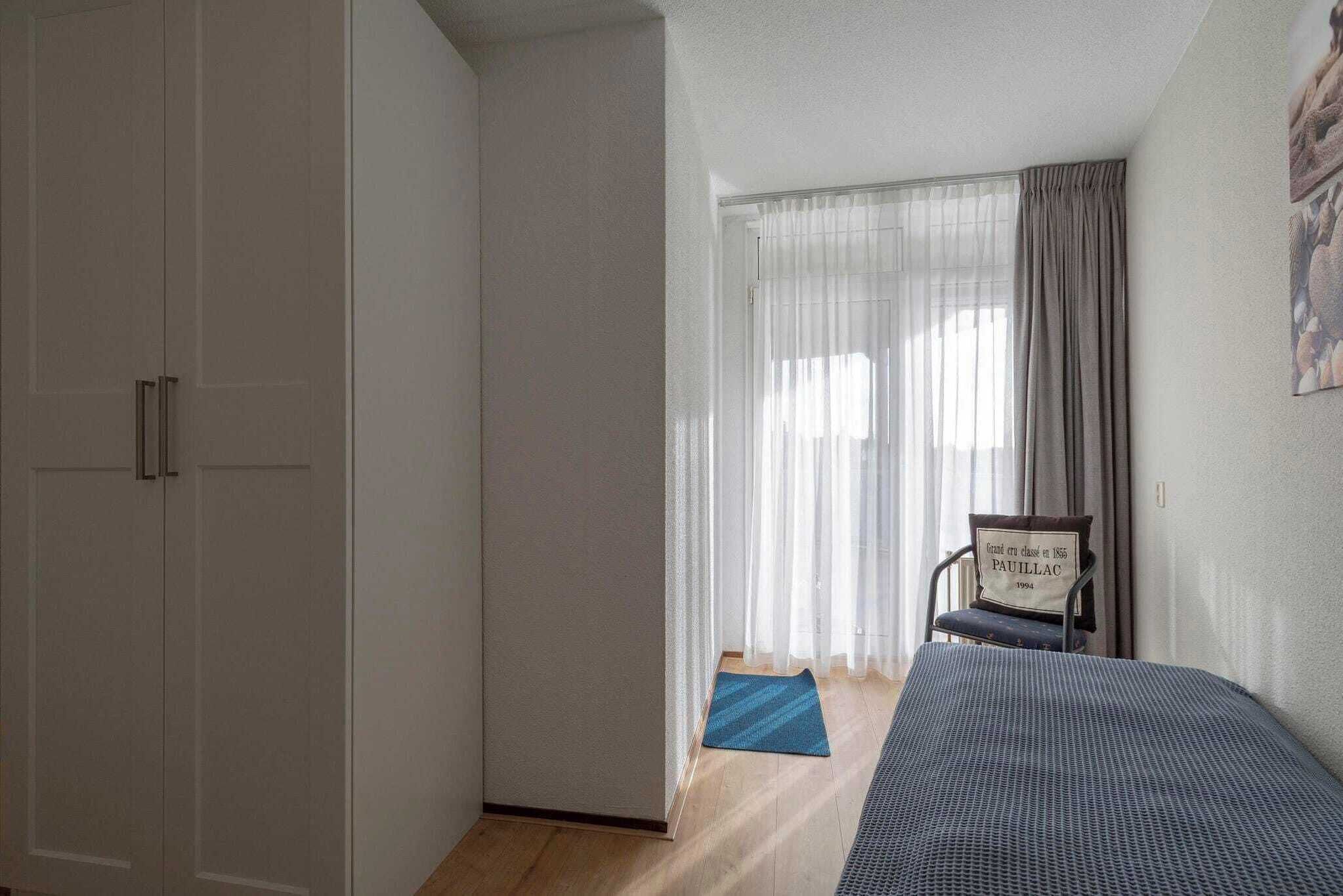 Een slaapkamer met een bed, een stoel, een kledingkast en een raam met gordijnen.