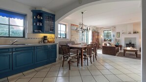 A spacious kitchen with blue cabinets, a dining area with a wooden table and chairs, and a living room with a fireplace. - De Buitenplaats 145 villa with sauna (Callantsoog)