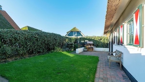 A courtyard with a thatched-roof house, a paved patio, and a hedge. - De Buitenplaats 145 villa with sauna (Callantsoog)