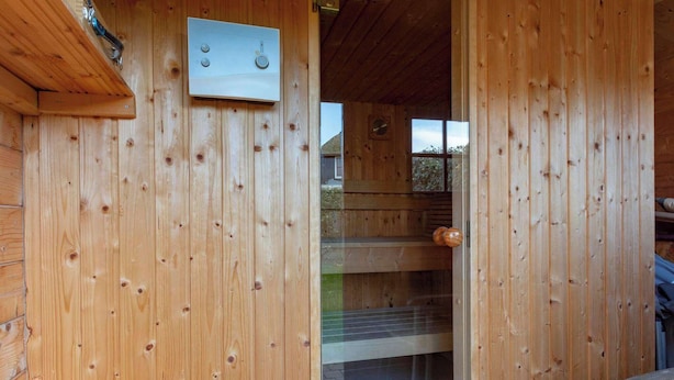 A wooden cabin with a wooden door, a small window, and a thermostat on the wall. - De Buitenplaats 145 villa with sauna (Callantsoog)